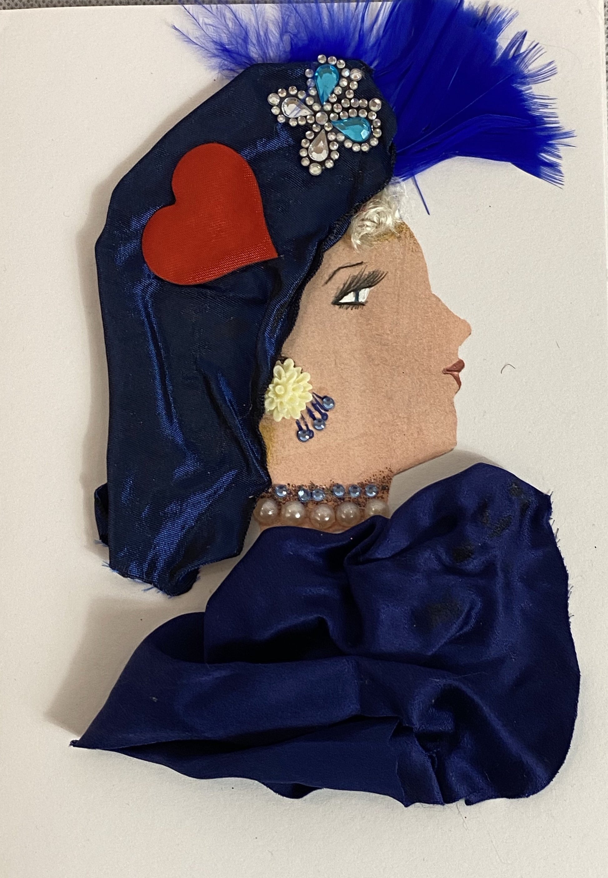 This card shows a woman wearing a dark blue silk dress. She wears a matching hat which has a red heart, diamond butterfly, and a blue feather on it. 