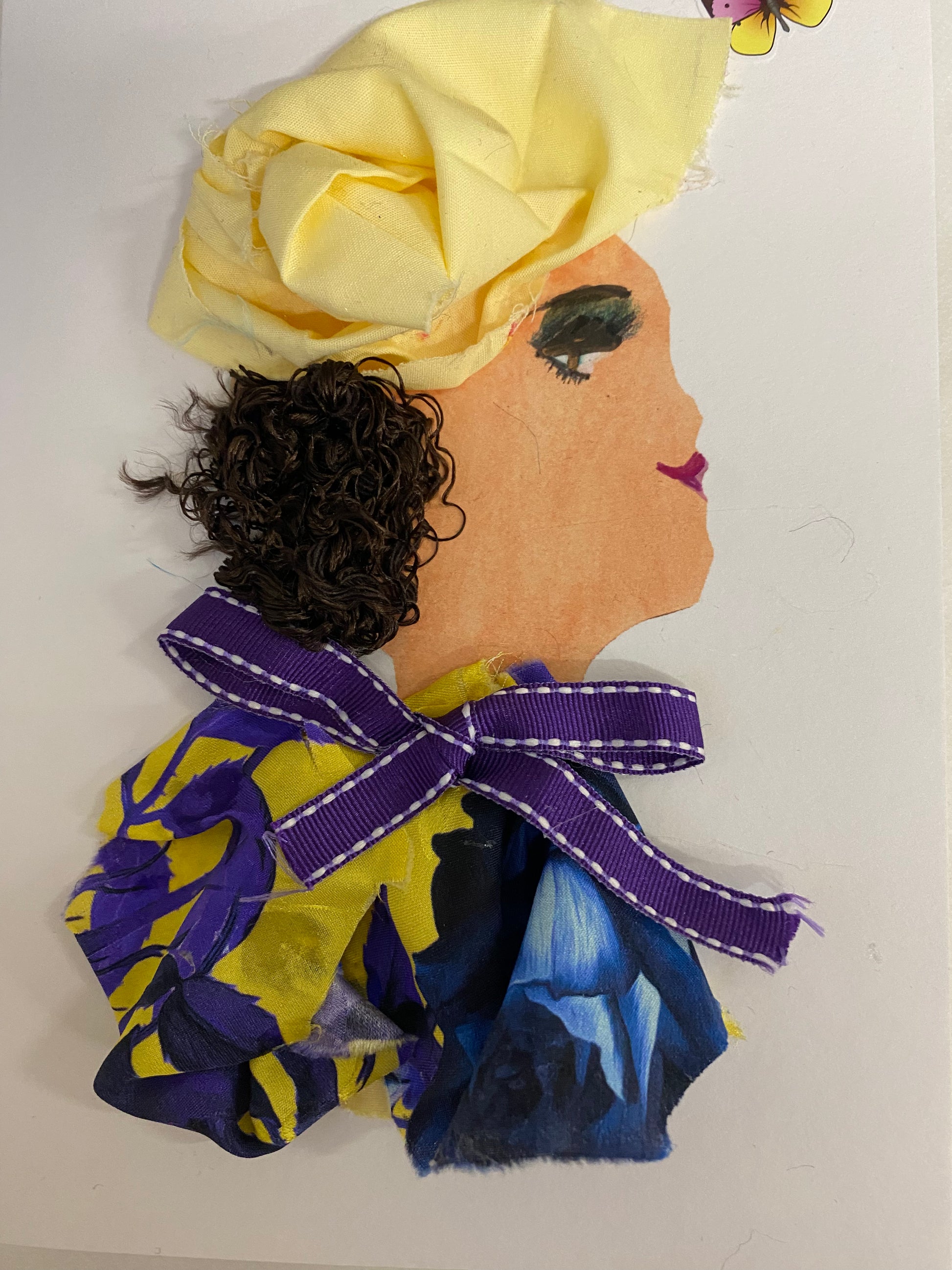 I designed this card of a woman who is wearing a bright yellow hatinator. She wears a colourful blouse tied together by a purple ribbon. Above her head there is a purple and yellow flower. 