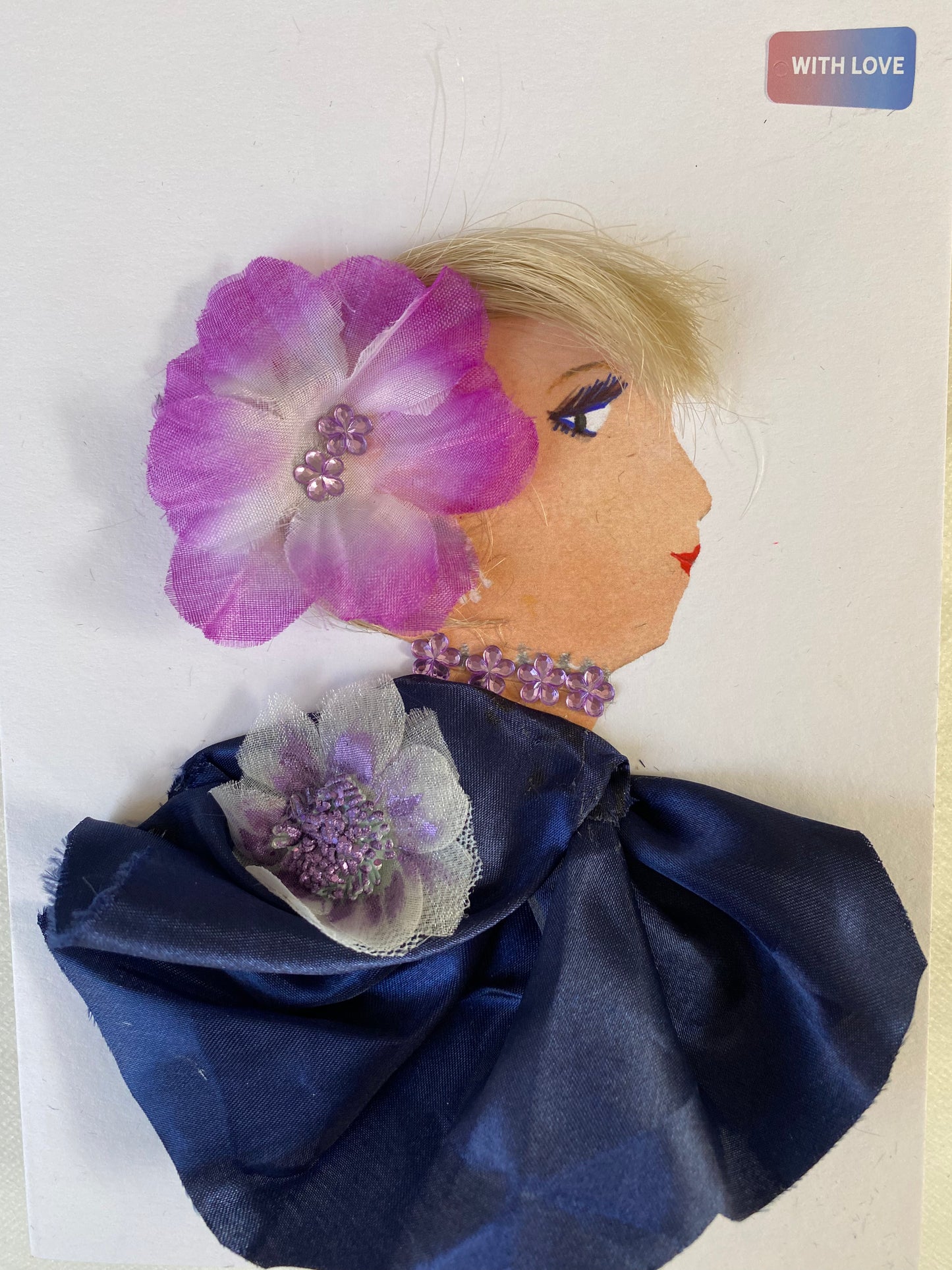 I designed this card of a woman named Dalston Doodle. She has a white skin tone and is wearing a stunning purple flower in her hair. She wears a silky blue blouse with a purple and white flower. She wears shiny purple jewellery. 
