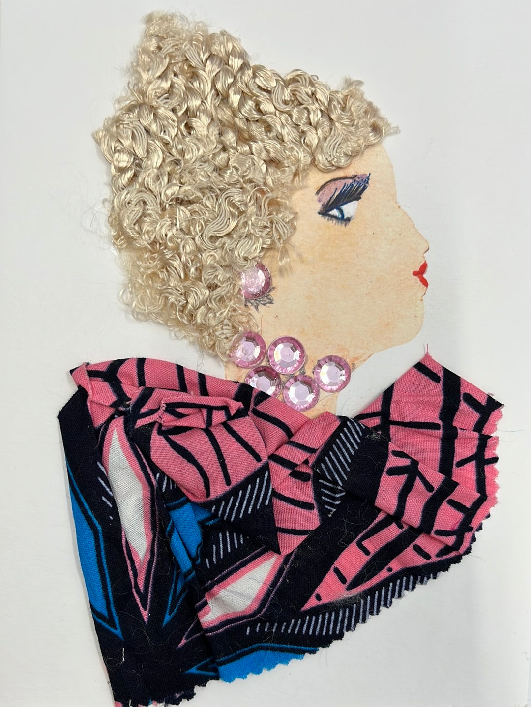 This card has been given the name Wilma Waterloo. Wilma wears a predominantly pink patterned blouse with black and sky blue accents. Her necklace and earrings are made of pink gems, and she has short, curly, blonde hair.