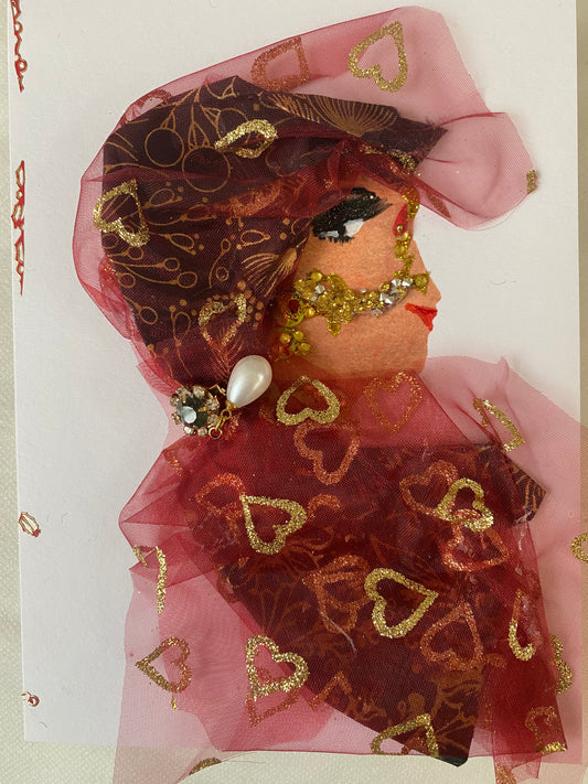 I designed this card of a woman named Ruby Rose. She has a white skin tone who wears an elegant red mesh hat with gold hearts. She wears a red blouse covered in dazzling gold hearts.  She is wearing gold bridal face jewellery called maang tikka. She also wears pearl earrings. 