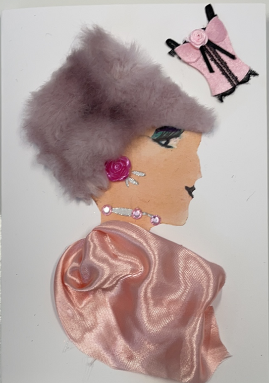 This card has been given the name Perivale. Perivale wears a salmon pink blouse that is a silken material, and her hair covered by a purple furry hat. She wears a pink rose earring, and a thin silver necklace with three pink gems. In the top right corner of the card, there is a sticker of a pink corset top which has a light pink rose on the bust.