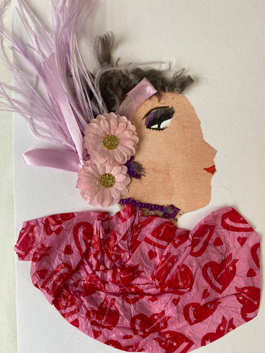 I designed this card of a woman named Carmen Cupcake. She has a white skin tone and headwrap that has two pink flowers with purple feathers. She wears a pink blouse with a red heart pattern. She wears shiny purple jewellery. 