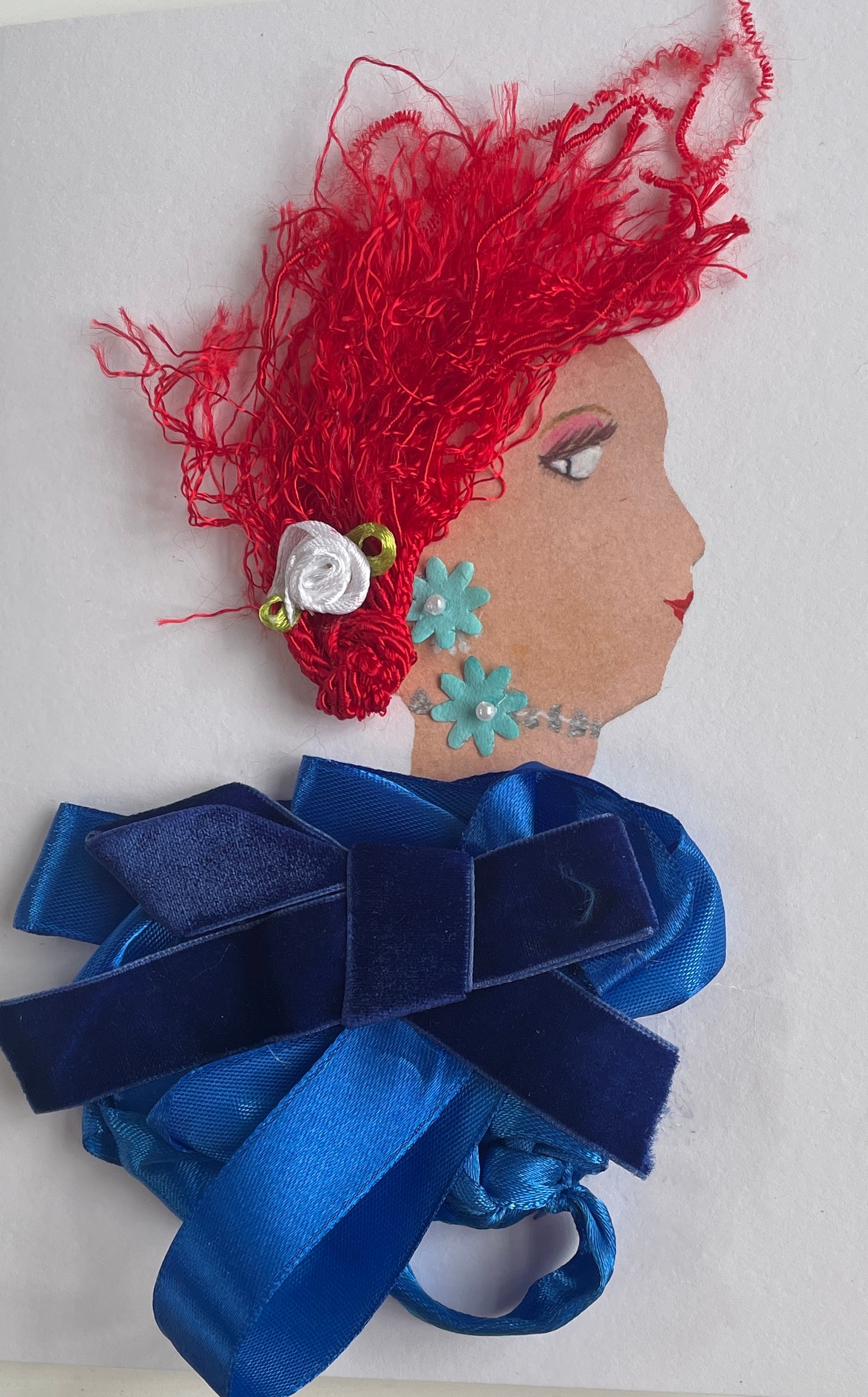 This card has been given the name Doncaster Darling. She wears a royal blue blouse made of satin type fabric ,and a darker blue velvet bow on top. Her hair is red and curly, and she has a small white rose in it. Her earrings are blue daisies and so is her necklace. A Good card to send or keep.
