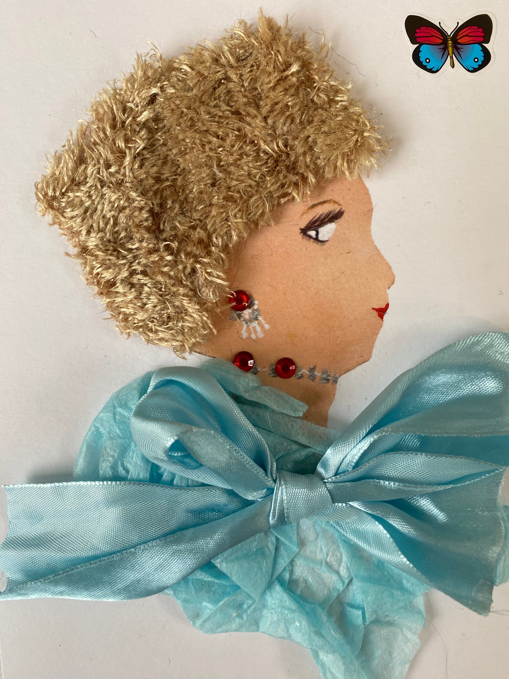 I designed this card of a woman who is wearing a beautiful warm fury blonde hat. She wears a baby blue silk blouse with a big bow on the front. She wears silver and red jewellery. In the corner there is a red and blue butterfly. 