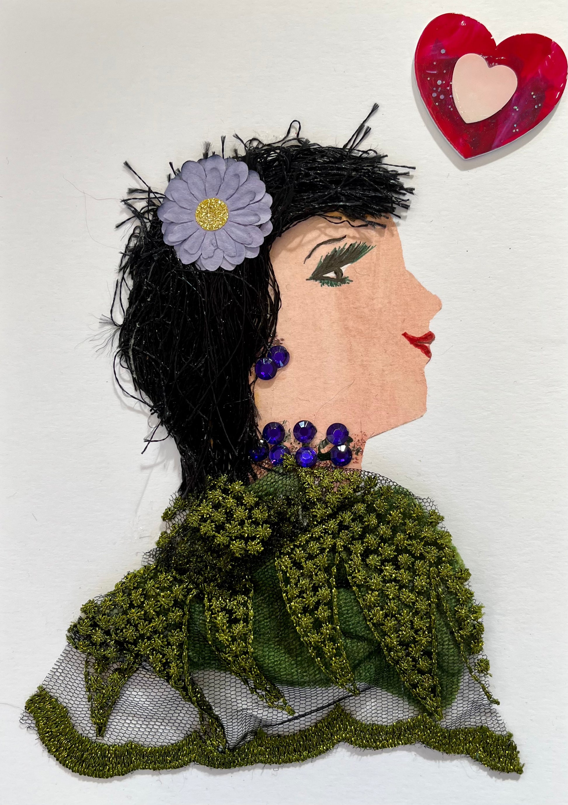 This card has been given the name Mish. Mish wears an olive green lace blouse, purple gem jewellery, and a purple flower with a gold center in her black hair. In the top right corner, there is a red heart. 